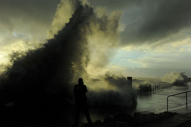 Một người dân ghi lại hình ảnh bầu trời đen kịt và sóng lớn xô bờ. Ảnh: PA