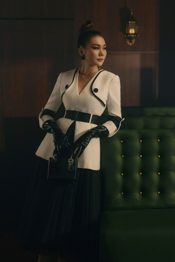 Thanh Hằng chọn thiết kế màu trắng với chất liệu vải tweed cùng sự nhấn nhá từ đường gân kẻ đen hòa quyện. Chân váy xếp pli mang lại sự mềm mại cần thiết và hài hòa với tổng thể. Trong khi đó, phụ kiện gang tay da cùng túi hiệu Dior Lady như khẳng định sự quyền lực