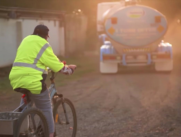 Anh Ken đạp xe theo sau chiếc xe tải thu gom sữa.