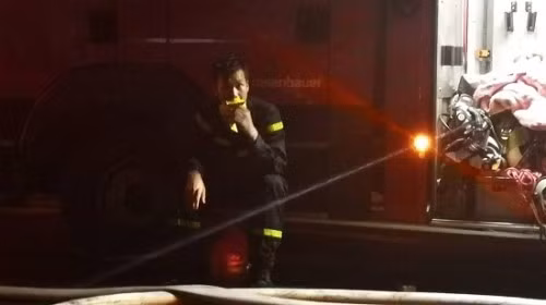 Một chiến sĩ ngồi cạnh chiếc xe cứu hỏa ăn vội chiếc bánh mì.