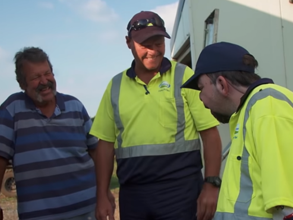 Bác Ken (bên trái) đứng chờ trong khi anh Andrew (bên phải) chào người lái xe tải thu gom sữa.