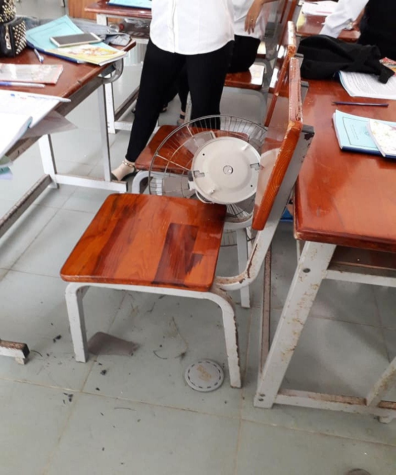 Chiếc quạt treo tường rơi giữa ghế ngồi của 2 bạn sinh viên.