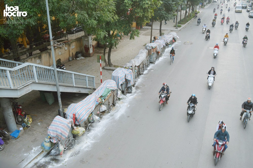 Gần 20 chiếc xe chở rác nối liền nhau trên đường Nguyễn Trãi, Thanh Xuân, Hà Nội. Nhân viên môi trường đã tạm thời xử lý rác bằng cách lấy bạt che và rắc vôi bột lên để hạn chế mùi hôi của rác.
