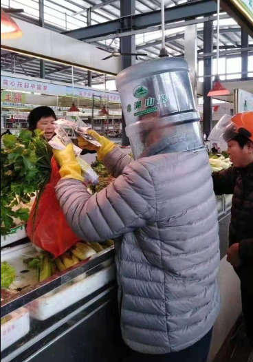 Đi găng tay cao su, đeo khẩu trang thôi vẫn chưa đủ, người đàn ông này còn đội cả một chiếc thùng nhựa hình trụ trên đầu nữa, trái ngược hoàn toàn với người bán hàng, người không đeo khẩu trang.