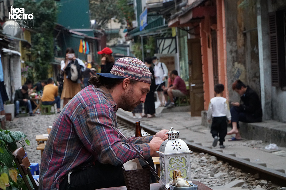 Chọn một chỗ ngồi ngay đường tàu,ngắm nhìn khung cảnh đông vui náo nhiệt trong khu xóm nhỏ là một trải nghiệm thú vị.