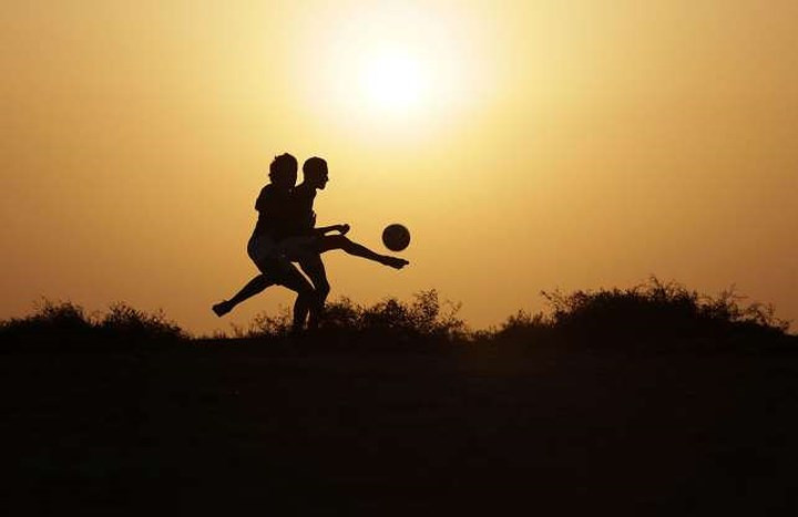 Các cậu bé chơi bóng trên một cánh đồng trong buổi chiều ở Malkiya, Bahrain.