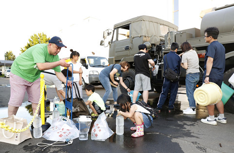 Một số người tranh thủ hứng nước từ các xe bồn ở thị trấn Atsuma. Ảnh: REUTERS.
