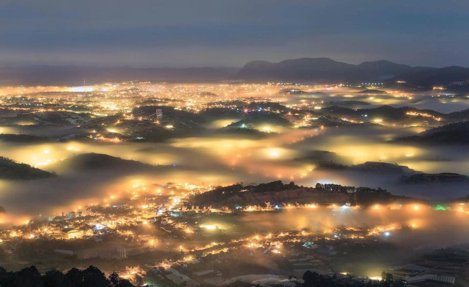 Thành phố chìm trong sương mờ với ánh đèn vàng lung linh, ấm cúng.