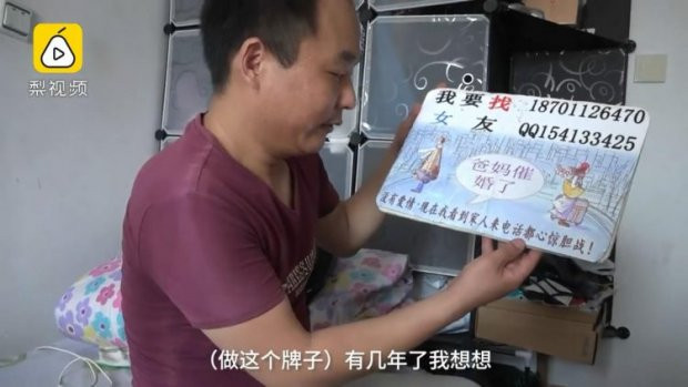 Anh Niêu cùng tấm biển tìm vợ. Ảnh: Pear video.