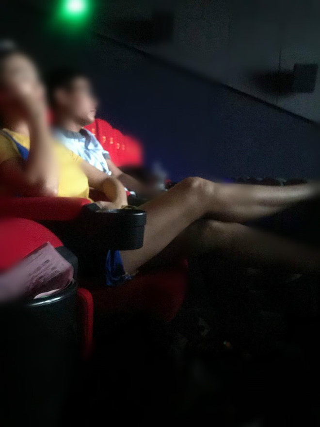 Bạn nữ ngồi chiếm chỗ, gác chân lên ghế trong rạp chiếu phim.