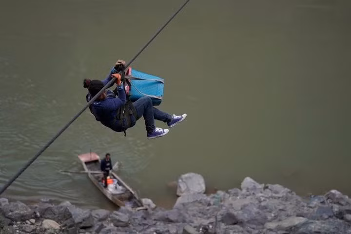 Một phụ nữ Lật Túc khác từ làng Lazimi đu dây qua sông Nộ. Tay chị xách theo một cái làn.