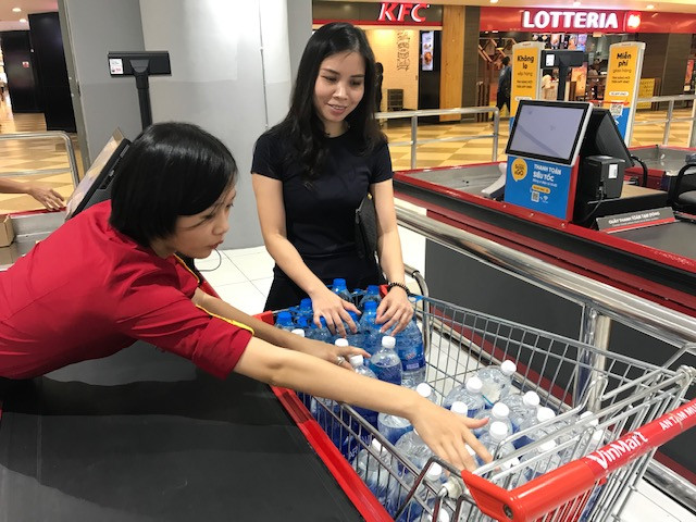 Nhân viên siêu thị đang đếm các chai nước loại 1,5 lít trong xe đẩy của một khách hàng