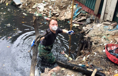 Người đàn ông nước ngoài mặc đồ bảo hộ lội xuống cống vớt rác.