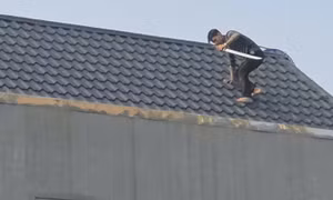 Một trong 2 người đàn ông cầm kiếm cố thủ trên mái nhà.