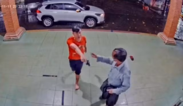 Người mặc áo đỏ cầm vật giống cây súng chĩa vào hai phụ nữ đối diện - ảnh chụp màn hình