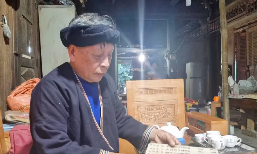 Nghệ nhân Lý Văn Hềnh đang lật từng cuốn sách cổ viết bằng giấy dó mà người xưa để lại