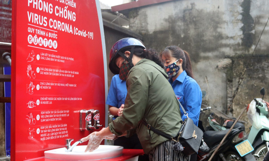Đoàn viên thanh niên hướng dẫn người dân rửa tay đúng cách và tuyên truyền phòng chống dịch. Ảnh: TĐHG
