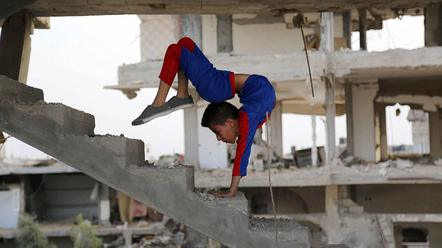 Bộ trang phục màu xanh đỏ, tươi sáng của cậu nổi bật giữa đống đổ nát xám xịt. 