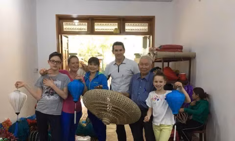 Cụ Huỳnh Văn Ba chụp hình lưu niệm với du khách tại xưởng đèn lồng của gia đình