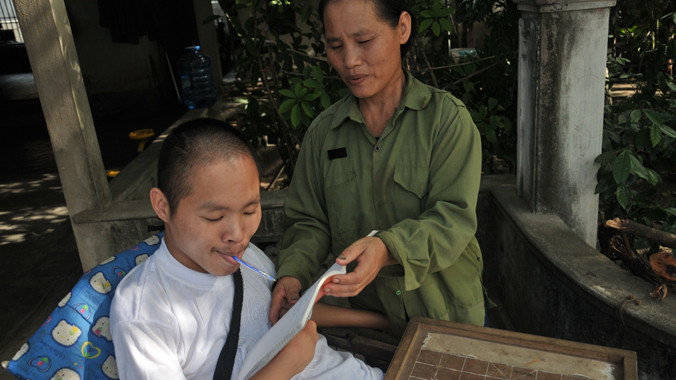 Bà Trần Thị Hà đang giữ sách để con viết. Ảnh: Quang Long