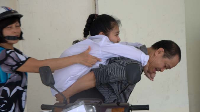 Thí sinh Mai Phương bị chứng chậm phát triển hệ thần kinh vận động bẩm sinh khiến xương rất mềm, không thể tự đi lại, mà phải nhờ vào bố mẹ cõng đến trường thi Học viện Bưu chính viễn thông ngày 5/7. Ảnh: Hồ Thu