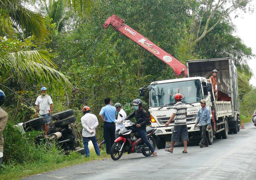 Chiếc xe tải nằm gọn dưới kênh và người dân phụ giúp chuyễn hàng lên bờ.