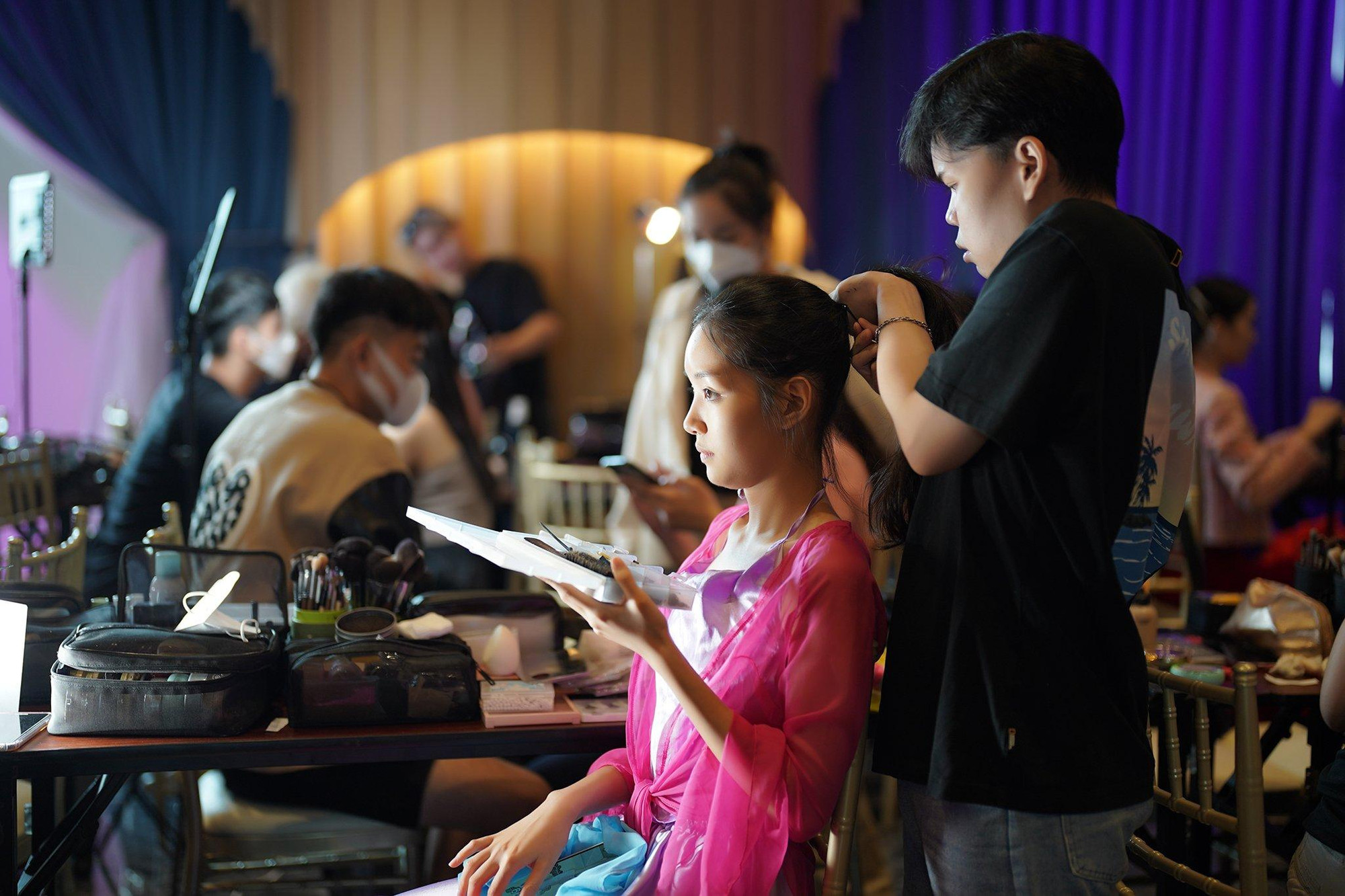 Thí sinh Trần Lê Mai Chi &quot;giúp đỡ&quot; thành viên ê-kíp trang điểm trong lúc họ bận làm tóc cho cô.