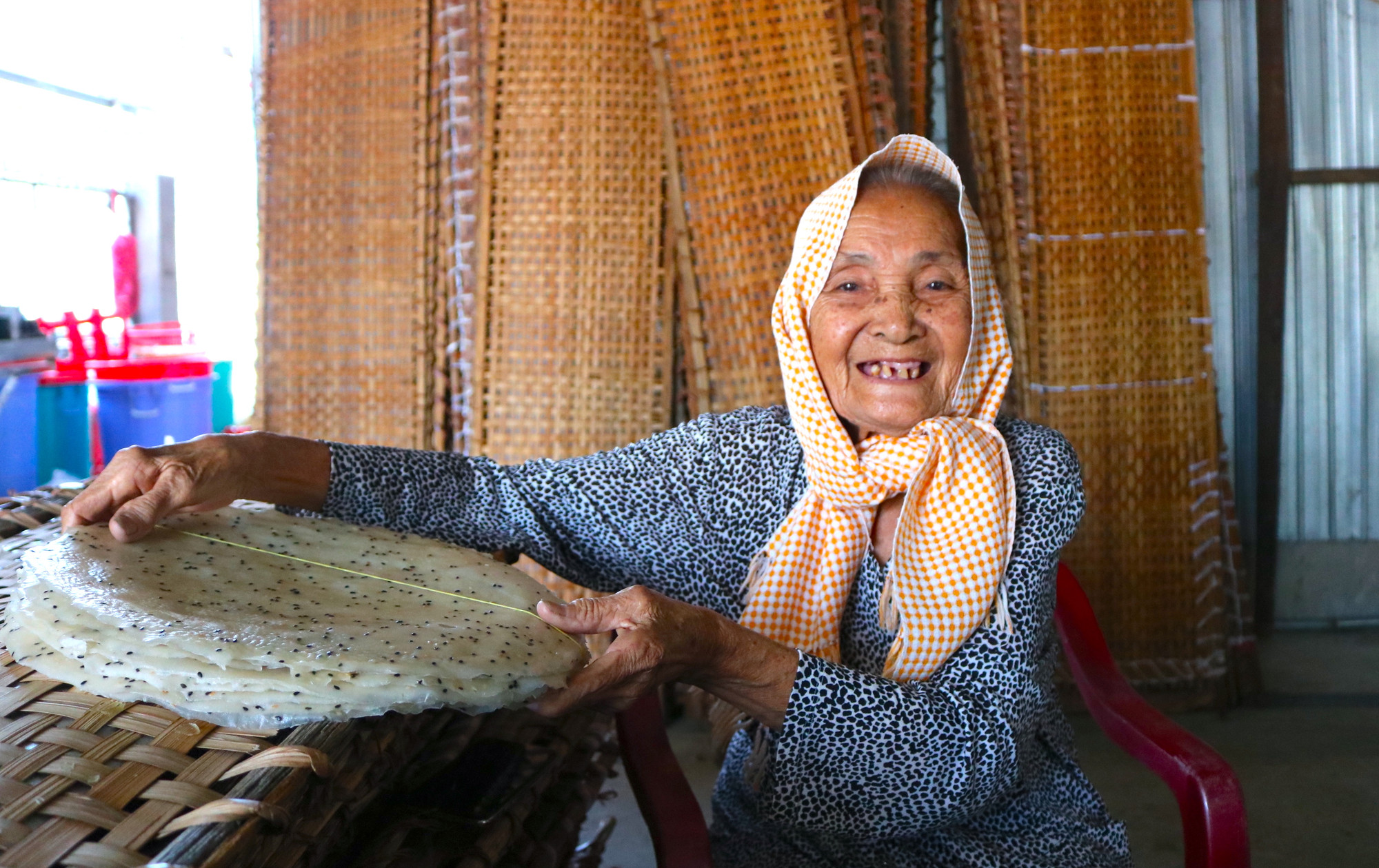 Có tuổi nghề hơn 30 năm, cụ Đỗ Thị Đượm (88 tuổi, ngụ phường Thuận Hưng) nhớ về những ngày khi mới khởi nghiệp nghề làm bánh tráng với nhiều thăng trầm. "Nghề này cực khổ lắm. Hồi đó, gia đình nghèo, tôi phải đi cắt lúa mướn, rồi ở lại mót lúa còn sót lại, bắt cá cạn để về làm mắm ăn. Sau đó, con dâu tôi mới dành dụm tiền xây được cái lò, rồi tôi và con gái cùng làm. Mấy chục năm trước tráng có cái Tết, mà chỉ tráng bánh tráng mặn thôi. Còn bây giờ tráng quanh năm, rồi con gái tôi mới tráng thêm bánh tráng lạt, bánh tráng ngọt và bánh tráng dừa. Nhu cầu của khách hàng ngày càng nhiều, gần đây nó đầu tư thêm máy tráng để kịp sản xuất cung ứng", cụ Đượm tâm sự - Ảnh: Kim Hà. Có tuổi nghề hơn 30 năm, cụ Đỗ Thị Đượm (88 tuổi, ngụ phường Thuận Hưng) nhớ về những ngày khi mới khởi nghiệp nghề làm bánh tráng với nhiều thăng trầm. "Nghề này cực khổ lắm. Hồi đó, gia đình nghèo, tôi phải đi cắt lúa mướn, rồi ở lại mót lúa còn sót lại, bắt cá cạn để về làm mắm ăn. Sau đó, con dâu tôi mới dành dụm tiền xây được cái lò, rồi tôi và con gái cùng làm. Mấy chục năm trước tráng có cái Tết, mà chỉ tráng bánh tráng mặn thôi. Còn bây giờ tráng quanh năm, rồi con gái tôi mới tráng thêm bánh tráng lạt, bánh tráng ngọt và bánh tráng dừa. Nhu cầu của khách hàng ngày càng nhiều, gần đây nó đầu tư thêm máy tráng để kịp sản xuất cung ứng", cụ Đượm tâm sự - Ảnh: Kim Hà.