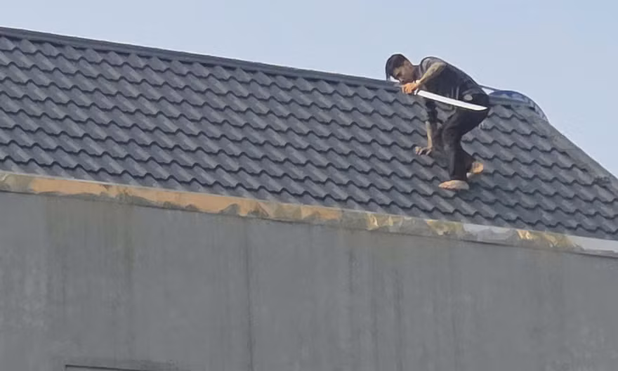 Một trong 2 người đàn ông cầm kiếm cố thủ trên mái nhà.