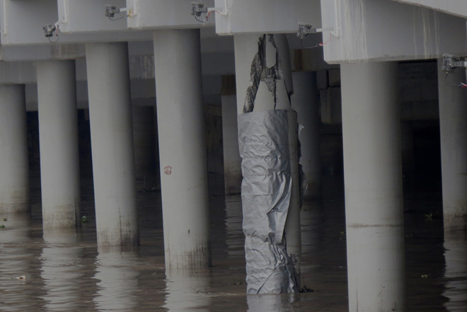 Trụ cầu được cuốn tấm bạt che chắn nhưng vẫn để lộ vết vứt vỡ, có thể nhìn thấy cả những thanh sắt bên trong. Ảnh: Tùng Chi.