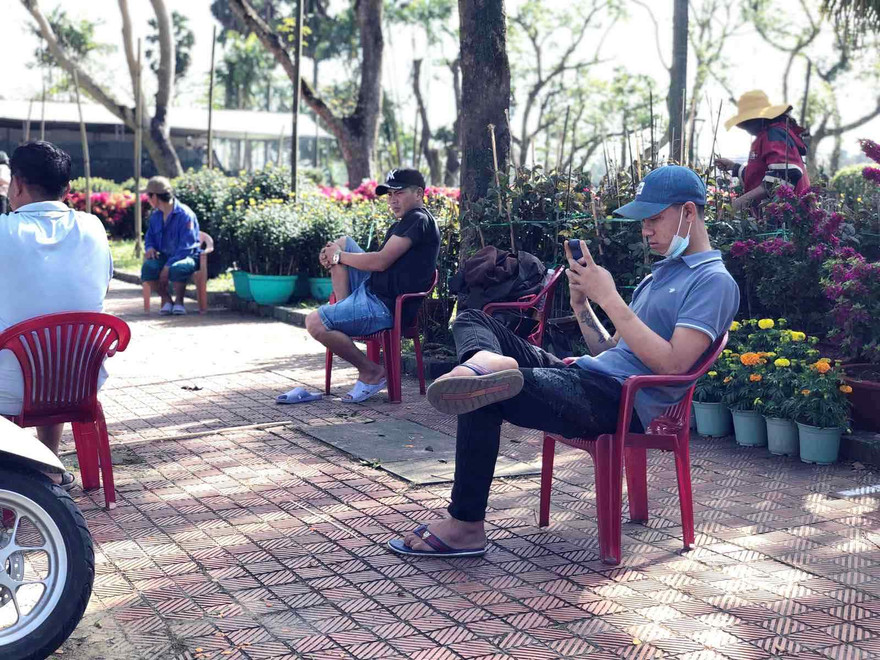 Vắng khách, người bán hoa Tết ngồi nghịch điện thoại giết thời gian.