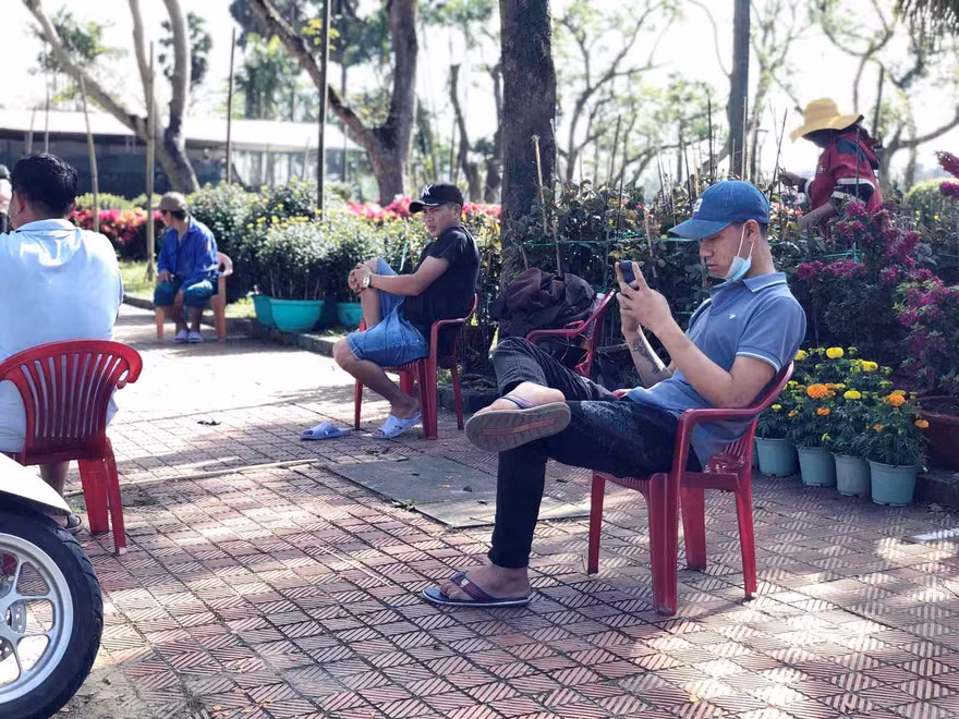 Vắng khách, người bán hoa Tết ngồi nghịch điện thoại giết thời gian.