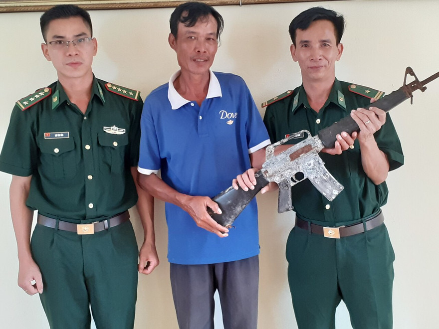Khẩu súng quân dụng do ngư dân Nguyễn Hậu Nghĩa (giữa) phát hiện trong lúc đánh cá vùng cửa biển.