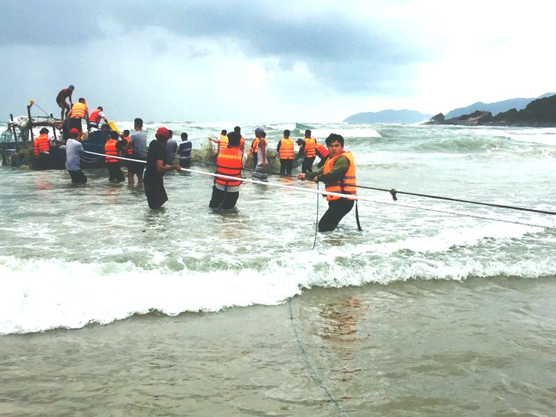 Lực lượng cứu hộ vật lộn sóng lớn nguy hiểm đưa ngư dân và chiếc thuyền chìm vào bờ an toàn (ảnh Ngọc Bình)
