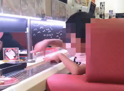 Một em bé đang bôi tay lên đĩa sushi di chuyển trên băng chuyền