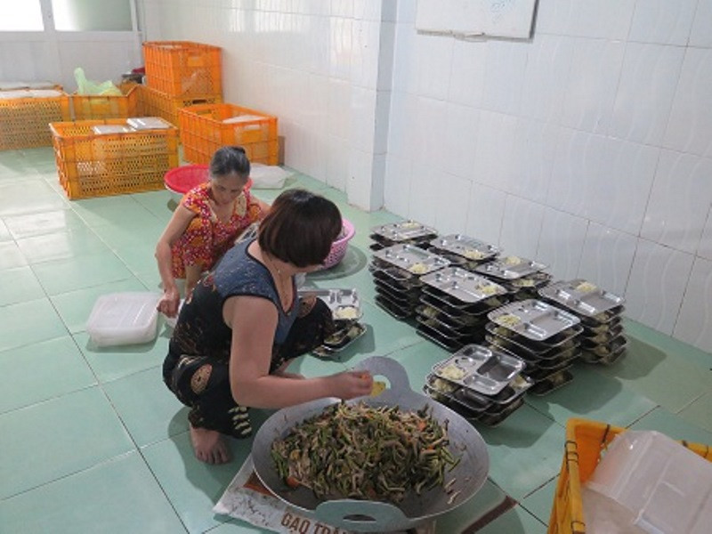 Nhân viên không có bảo hộ lao động đang múc thức ăn ra khay chuẩn bị giao hàng