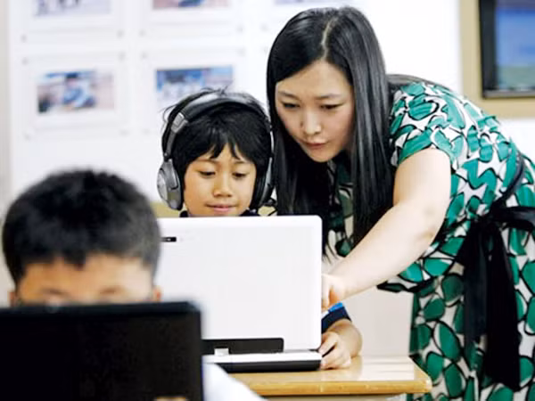 Giáo viên giúp HS học trên máy tính tại Trường tiểu học Sosu ở Gwesan (Hàn Quốc) - Ảnh: The Washington Post