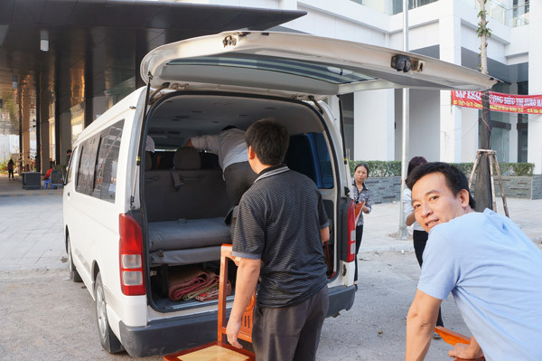 Một số người chuyển bàn ghế lên chiếc xe biển xanh
