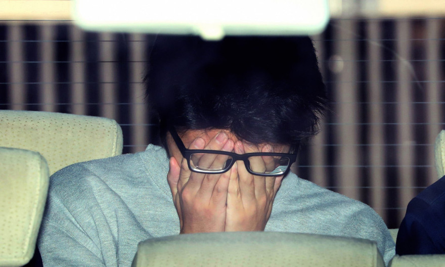 Bị cáo che mặt khi bị bắt tại đồn cảnh sát ở Tokyo. Ảnh: Ashahi Shinbum.