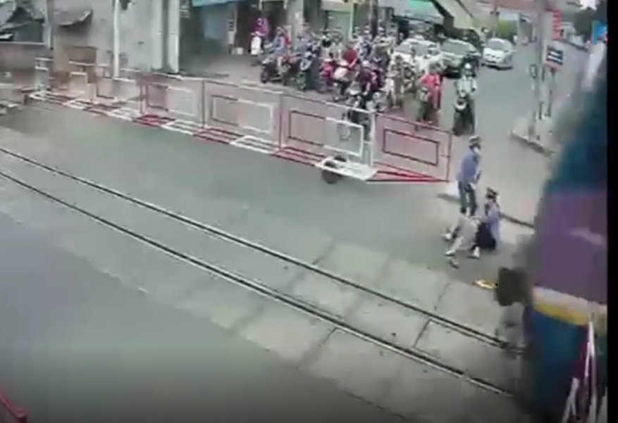 Cụ bà được 2 nữ gác chắn kéo ra khỏi đường sắt ngay trước mũi tàu. Ảnh cắt từ clip.