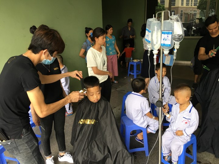 Nhiều bệnh nhi còn lủng lẳng bình dịch truyền xếp hàng ngồi chờ được cắt tóc. Ảnh: Đức Long