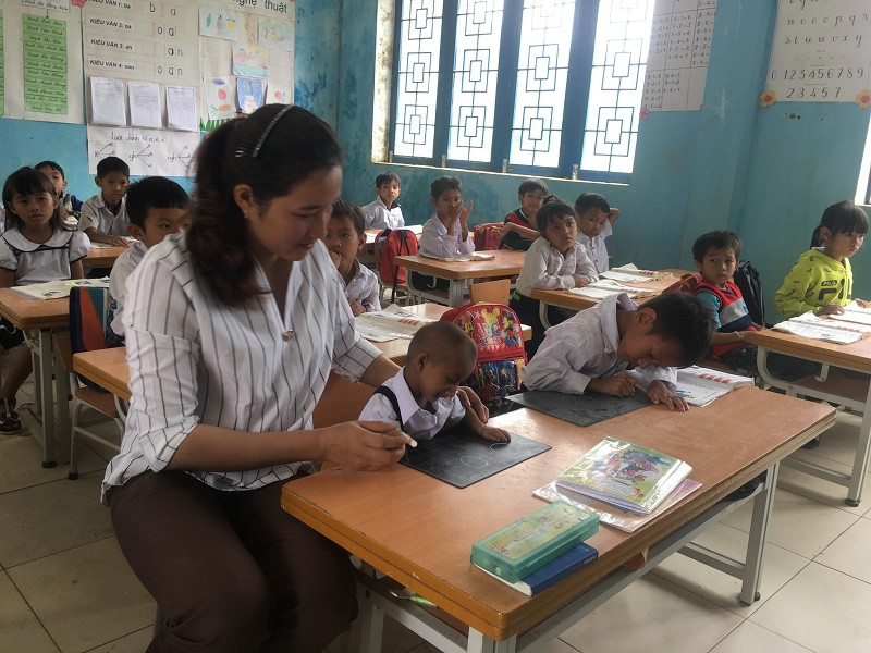 K'Rể đang được cô giáo chủ nhiệm dạy viết