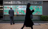 Một phụ nữ đi qua tấm bảng điện tử hiển thị chứng khoán Nhật Bản bên ngoài một công ty chứng khoán ở Tokyo ngày 20/3. (Ảnh: Reuters)