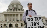 Một nhân viên liên bang Mỹ đứng ngoài tòa nhà Quốc hội giơ tấm biển có dòng chữ: “Hãy làm việc của các ông để tôi có thể làm việc của tôi”, sau khi chính phủ Mỹ bị đóng cửa tạm thời. Ảnh: Larry Downing.