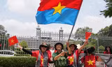 Người dân vẫy cờ Mặt trận Dân tộc Giải phóng miền Nam khi chụp ảnh trước Dinh Độc Lập ngày 29/4. (Ảnh: AP)
