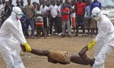 Các chuyên gia y tế đang di dời thi thể một người đàn ông chết vì nhiễm virus Ebola trước sự chứng kiến của đám đông tại thủ đô Monrovia của Liberia. Ảnh: AP