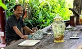 Anh Tuyền ngồi ngắm bình rượu sâm trên chiếc bàn gỗ hóa thạch khổng lồ, giữa khu vườn đầy hoa lá, chim muông 