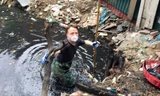 Người đàn ông nước ngoài mặc đồ bảo hộ lội xuống cống vớt rác.
