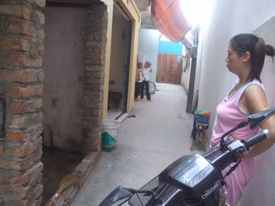 Chị Thơm đứng trước buồng chứa củi (có hai cột gạch không trát vữa), nơi phát hiện ổ bọ xít trên 1.000 con. 