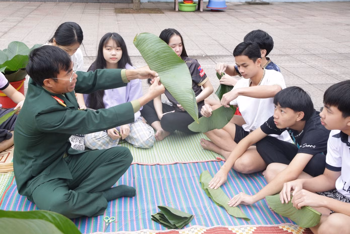 Các cán bộ chiến sĩ hướng dẫn từ việc chọn lá, cắt lá, chuẩn bị nguyên vật liệu đến việc gấp lá và gói bánh.